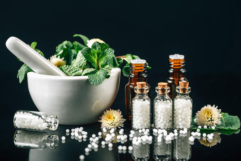 Homeopatski lekovi sa biljkama i globulama u mortu i bocicama na crnoj pozadini