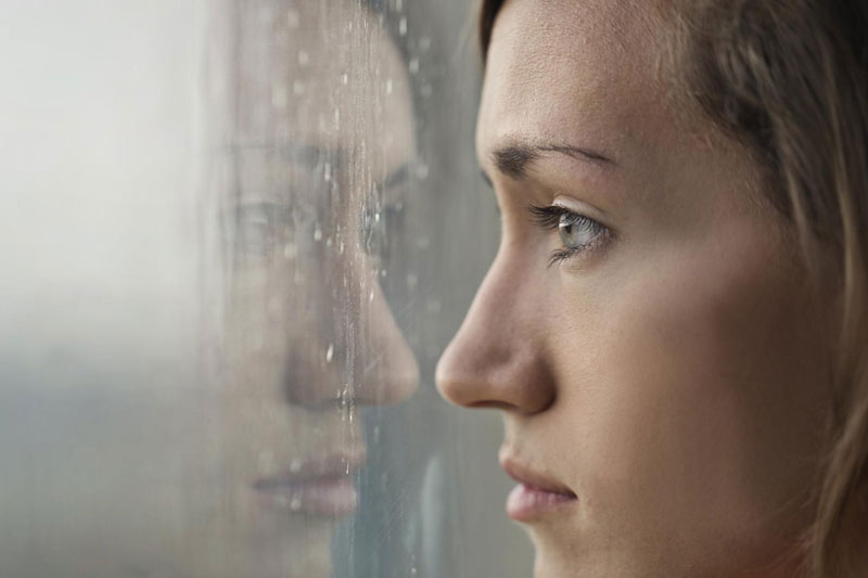 Žena zabrinuto gleda kroz prozor jer je muči socijalna fobija